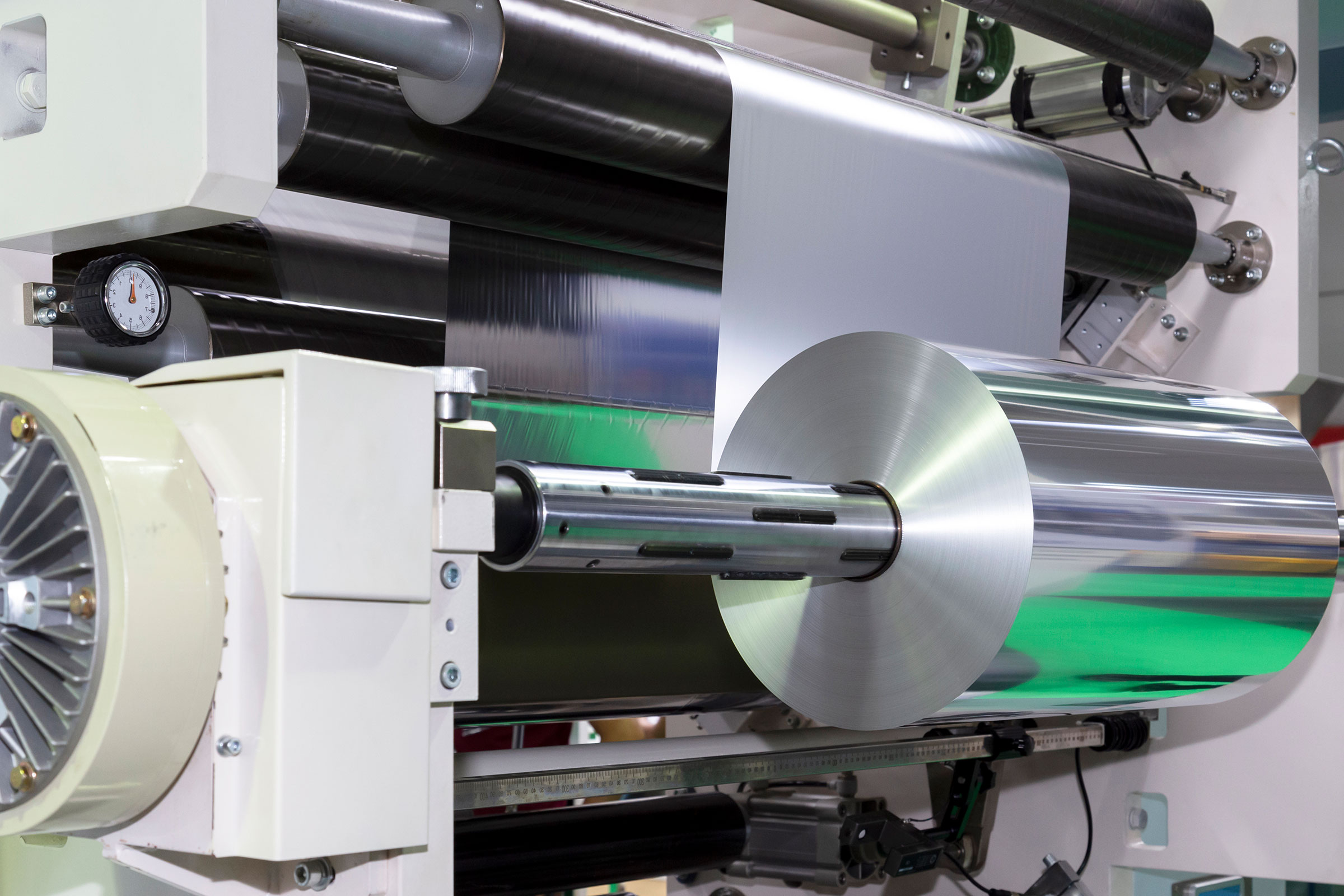 cirQum-audits-packmittel Maschine mit mehreren silbernen und schwarzen Walzen, auf der eine große Rolle Aluminiumfolie verarbeitet wird.