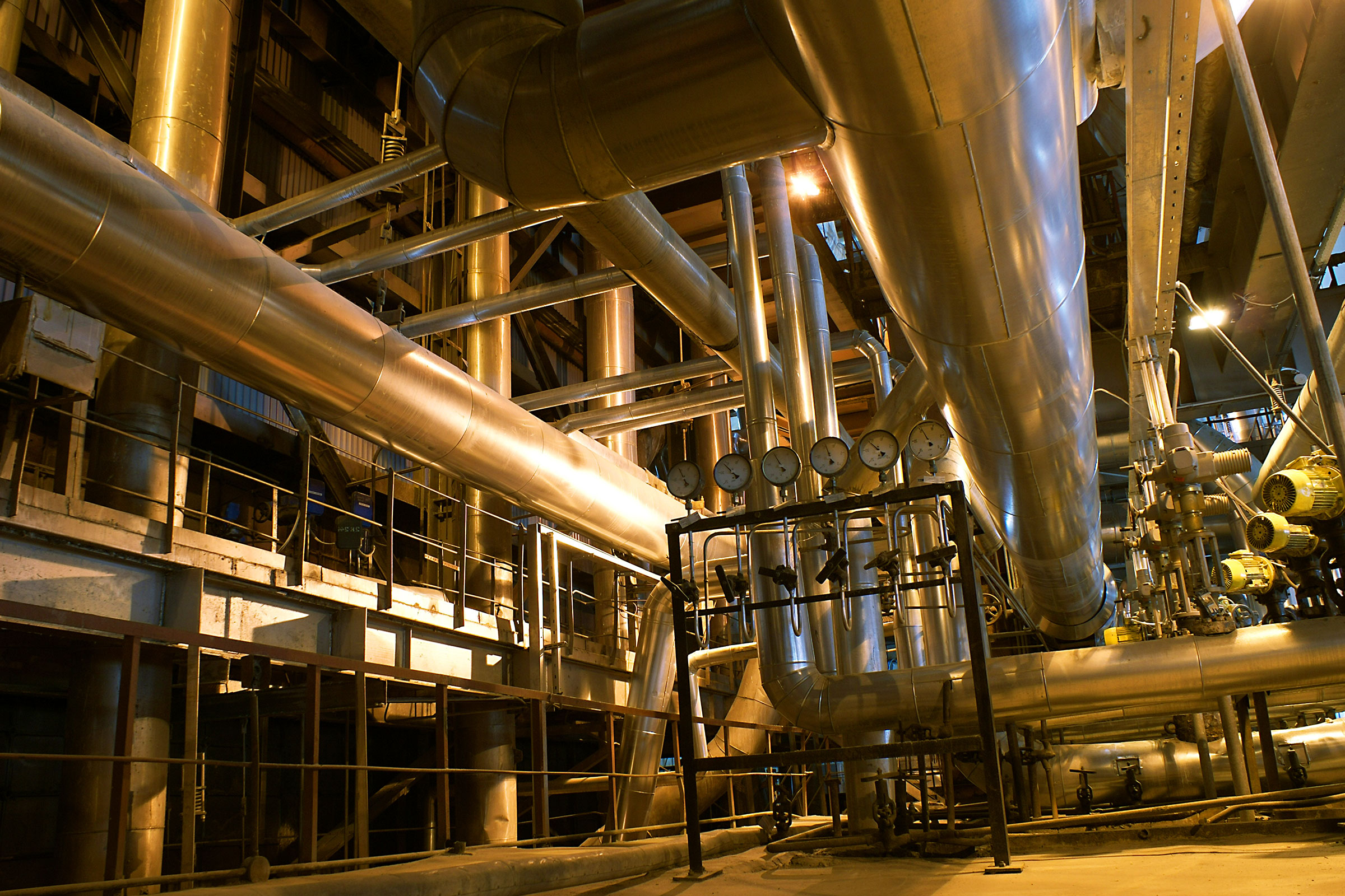 cirQum-audits-wirkstoffe Industrieanlage mit großen silberfarbenen Röhren und Manometern bei Nacht im Scheinwerferlicht.