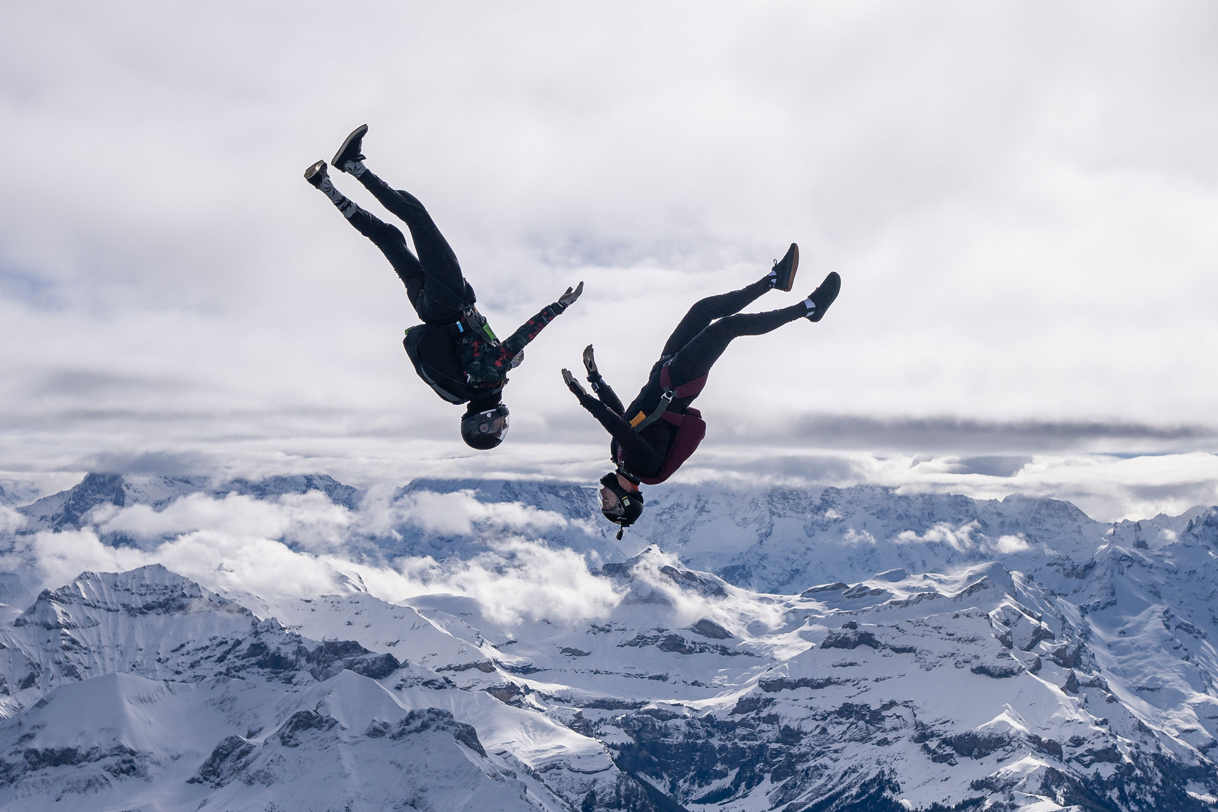 cirQum-beratung-risikomanagement Seitenansicht zweier Faltschirmspringer im freien Fall. Im Hintergrund ist eine schneebedeckten Berglandschaft zu sehen.