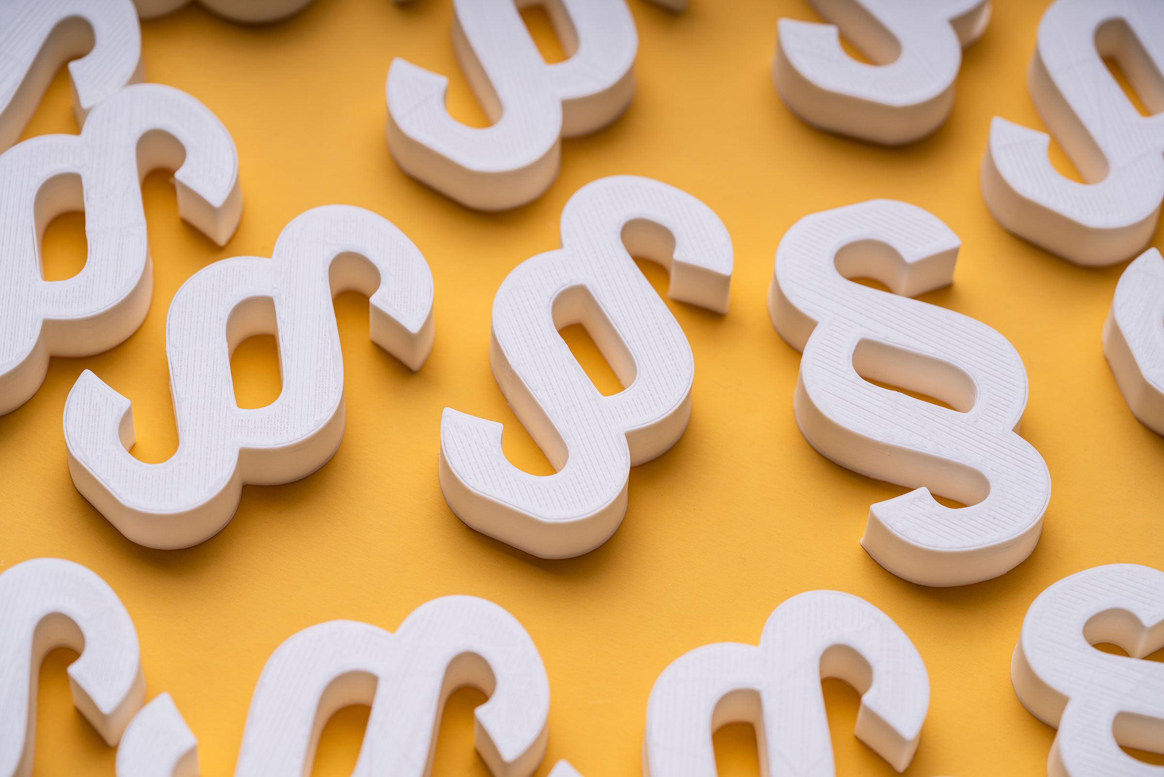 cirQum-cannabis-erlaubnisse Mehrere weiße Paragraphen-Zeichen liegen auf orangenen Fläche.