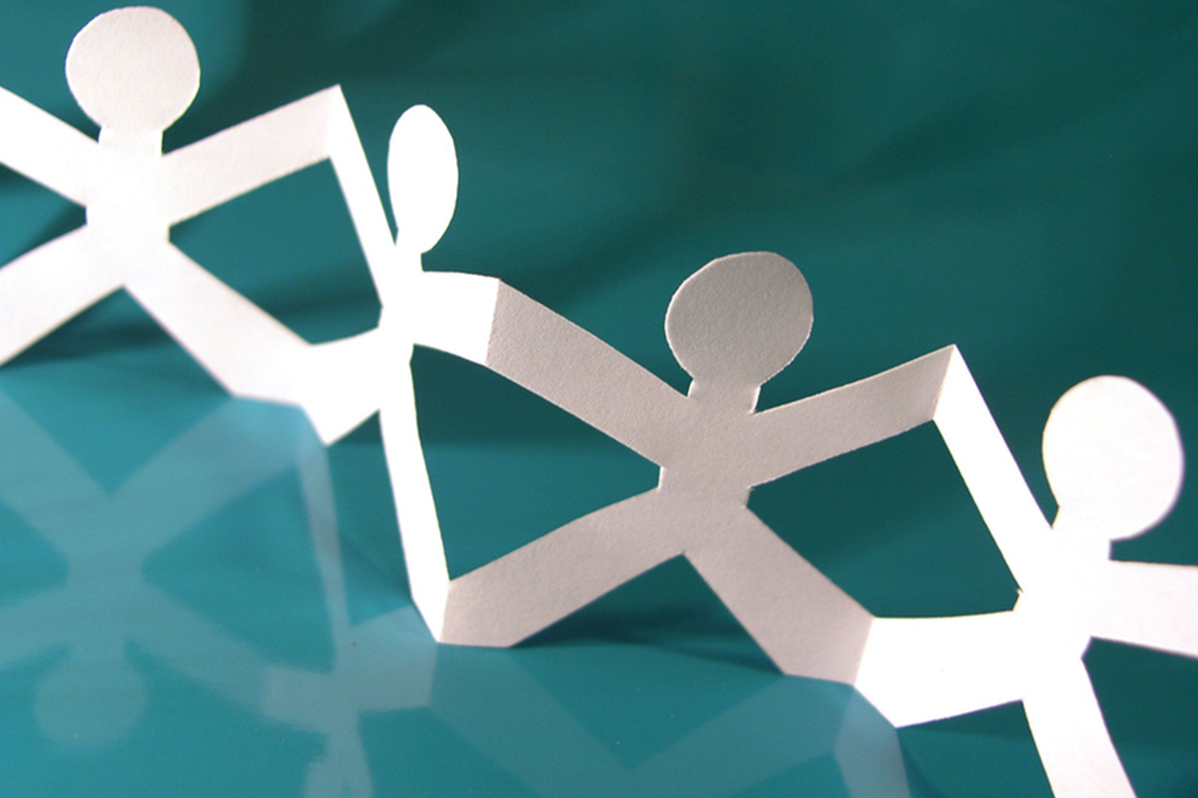 cirQum-schulungen-basisschulung Eine Papier-Menschenkette auf grünem Hintergrund.