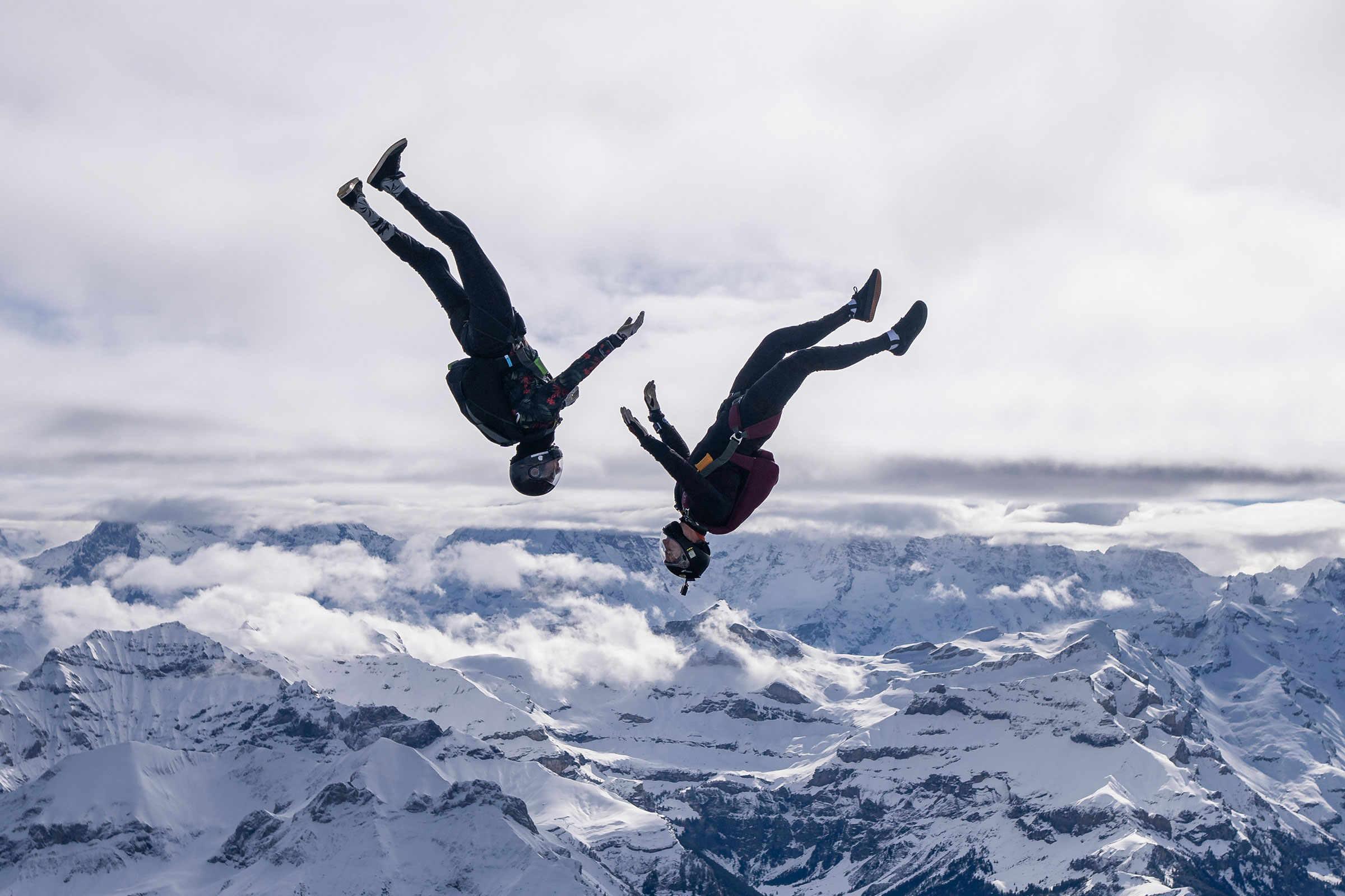 cirQum-schulungen-qrmursachenanalysen Seitenansicht zweier Faltschirmspringer im freien Fall. Im Hintergrund ist eine schneebedeckten Berglandschaft zu sehen.
